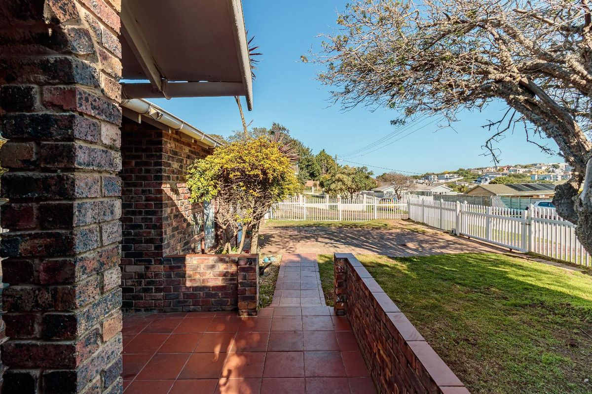 A view of the rear garden featuring a tiled patio area, brick retaining walls, and a white picket fence.