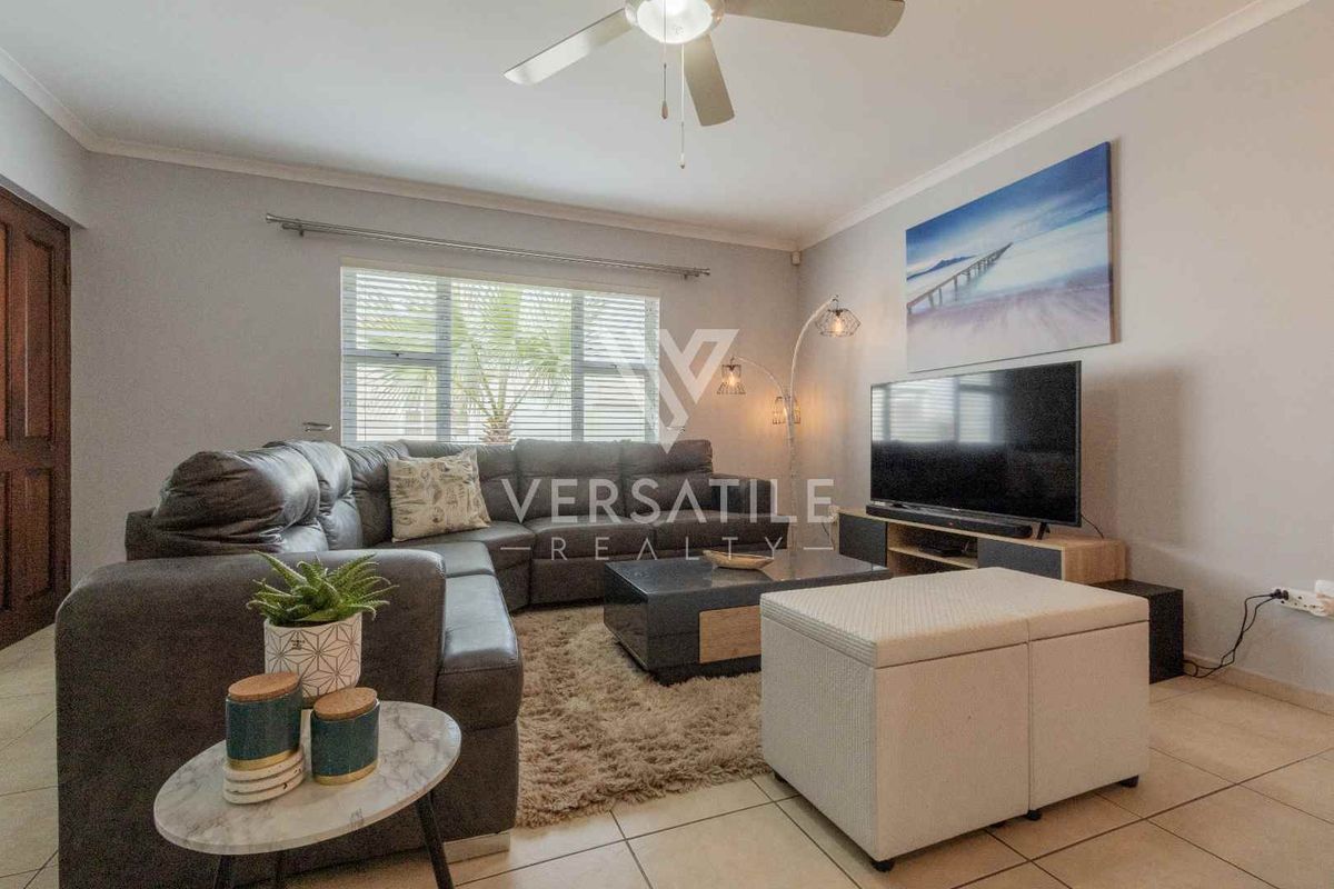 A comfortable living room featuring tiled flooring, a ceiling fan, and large windows that provide natural light.