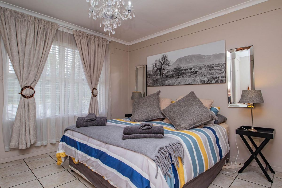 A well-lit bedroom featuring tiled flooring, a large window with curtains, and a decorative chandelier, providing a comfortable and functional living space.