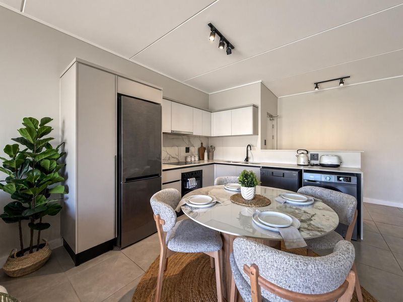 Modern open-plan kitchen featuring sleek cabinetry, integrated appliances, and tiled flooring, seamlessly flowing into a dining area with contemporary finishes.