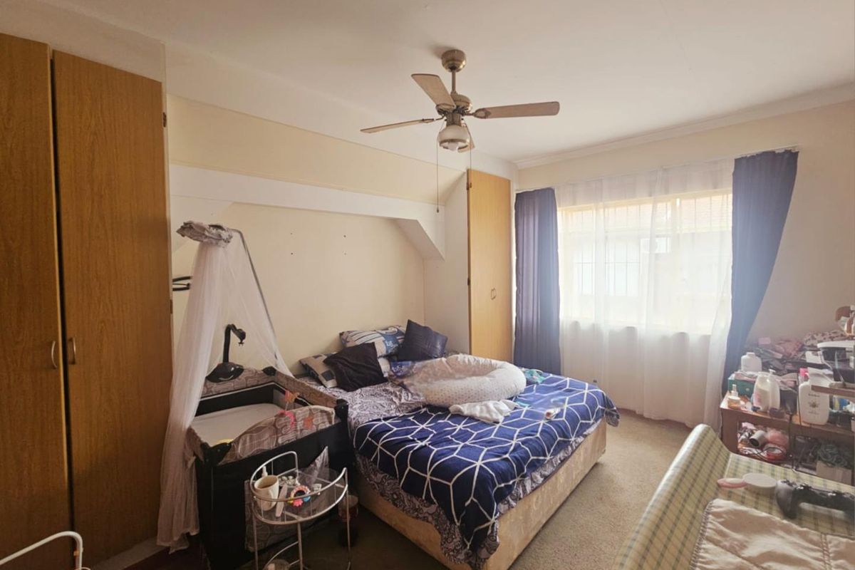 A bedroom featuring built-in wooden cupboards, a ceiling fan, and carpeted flooring, offering a functional space with natural light.