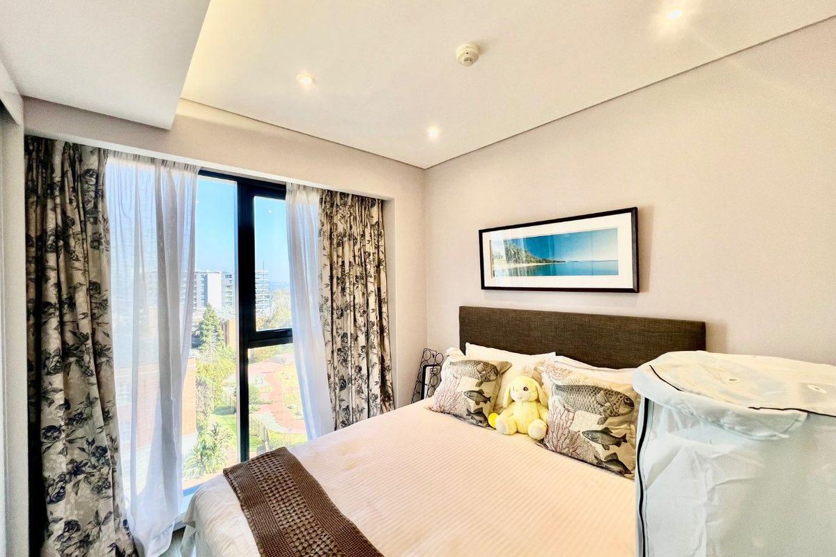 A bright and modern bedroom featuring recessed ceiling lighting, laminate flooring, and a large window offering pleasant exterior views.