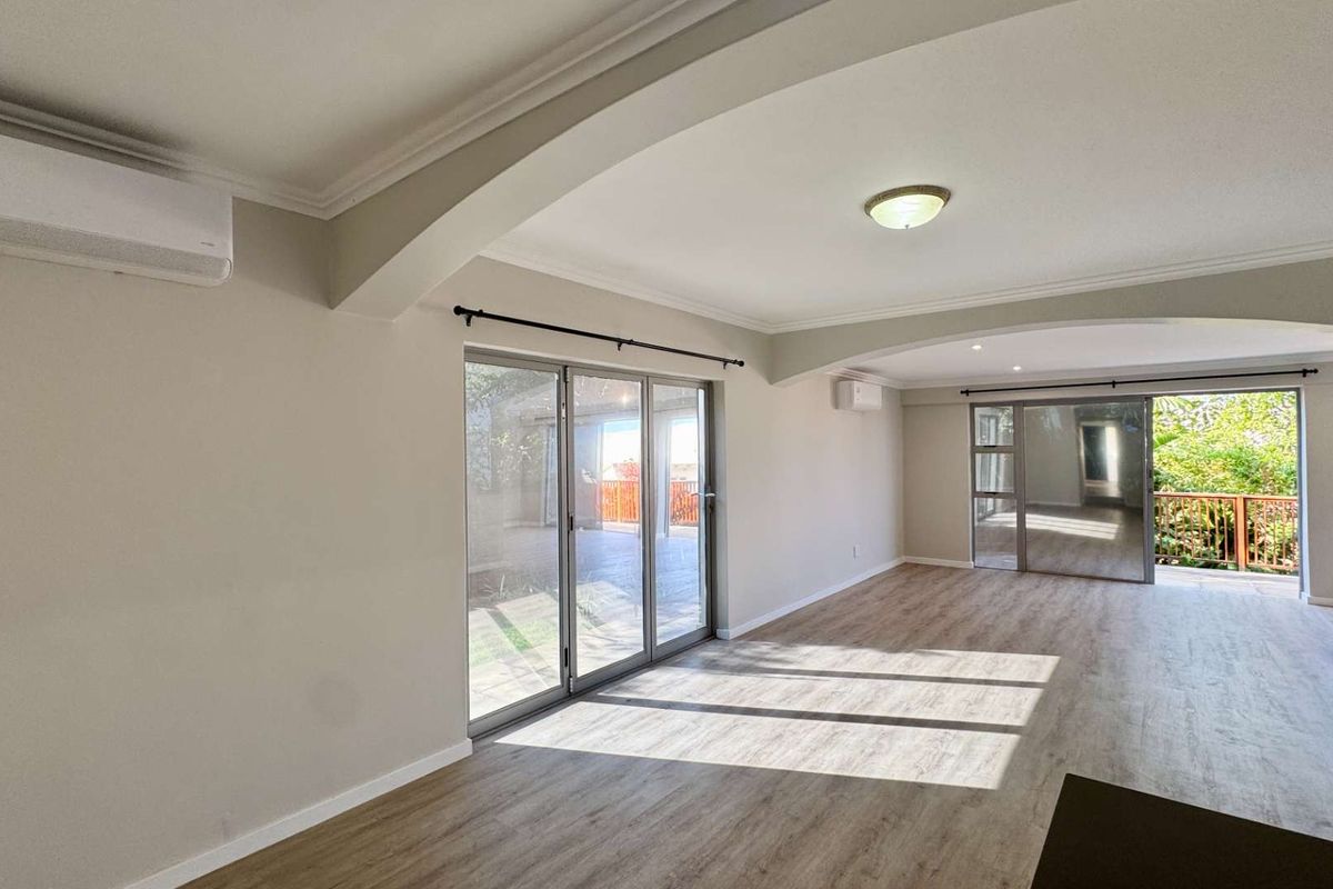 Spacious, light-filled living area featuring modern laminate flooring, split-system air conditioning, and large sliding glass doors opening to an outdoor space.