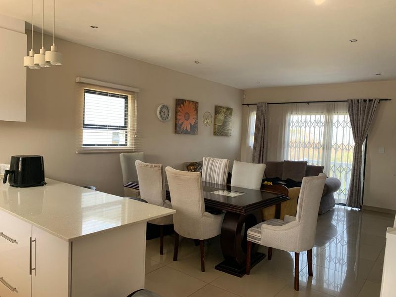 Open-plan living and dining area featuring tiled floors, recessed lighting, and a modern kitchen island with quartz countertops, leading to a patio through sliding doors.