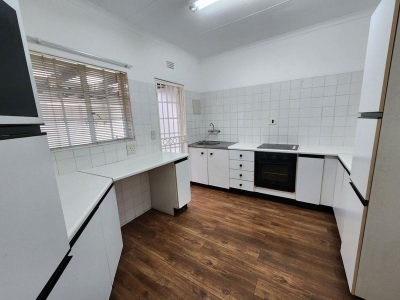 A functional kitchen featuring white built-in cabinetry, laminate countertops, a built-in oven with electric hob, and wood-look flooring.