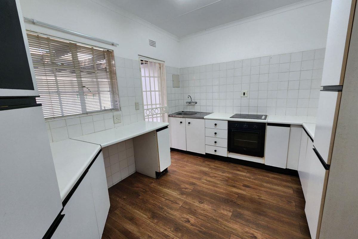 A functional kitchen featuring white built-in cabinetry, laminate countertops, a built-in oven with electric hob, and wood-look flooring.