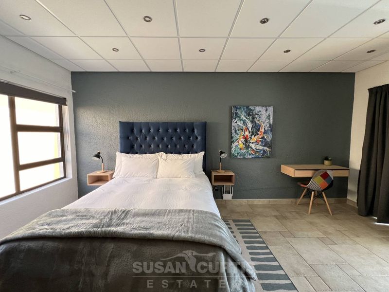 A well-lit bedroom featuring tiled flooring, a dark accent wall, and a suspended ceiling with recessed lighting.