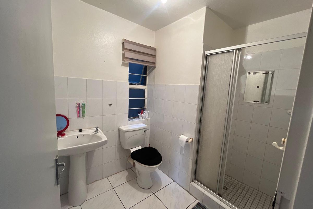 A functional bathroom featuring a pedestal sink, toilet, and a glass-enclosed shower with white wall and floor tiling.