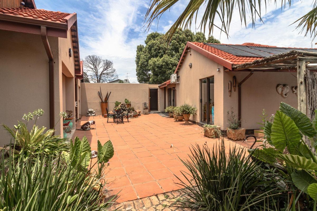 A spacious rear courtyard featuring terracotta tiling, established garden beds, and direct access to the home via glass sliding doors.
