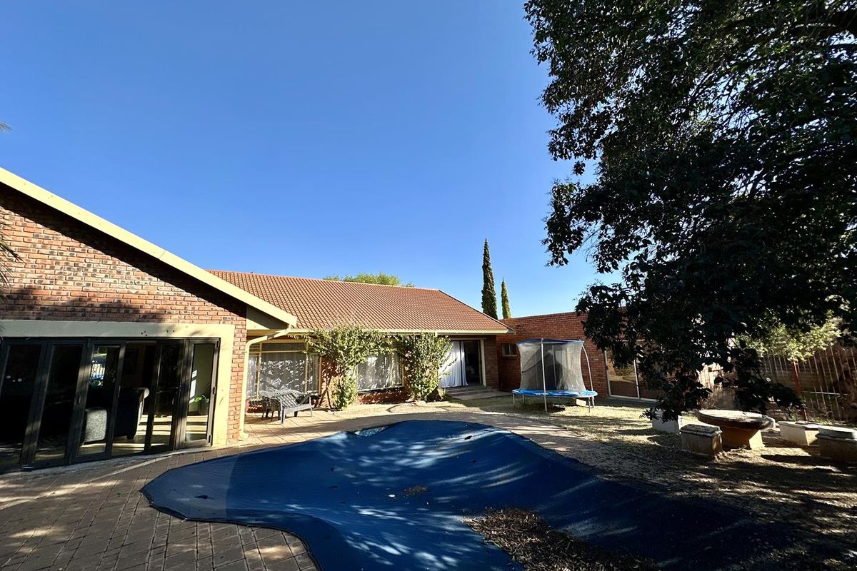 Rear exterior view featuring a paved patio area, swimming pool with cover, and brick house facade with sliding glass doors.