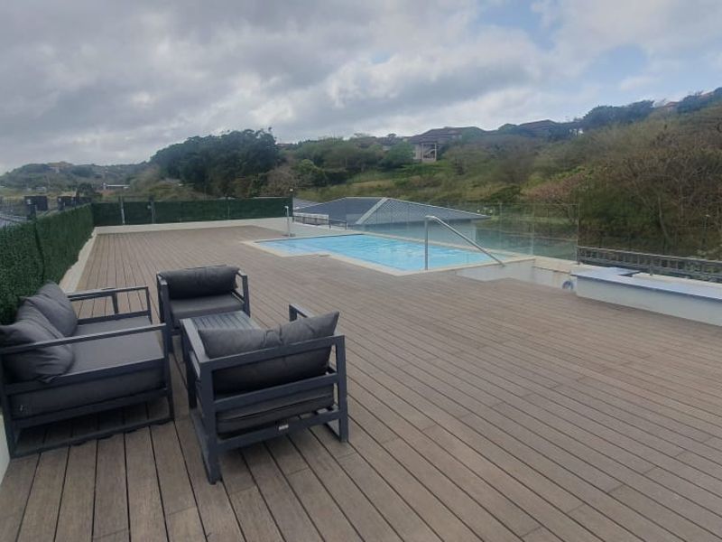 Spacious outdoor deck area featuring a swimming pool, glass balustrades, and artificial hedge privacy screening with scenic hillside views.