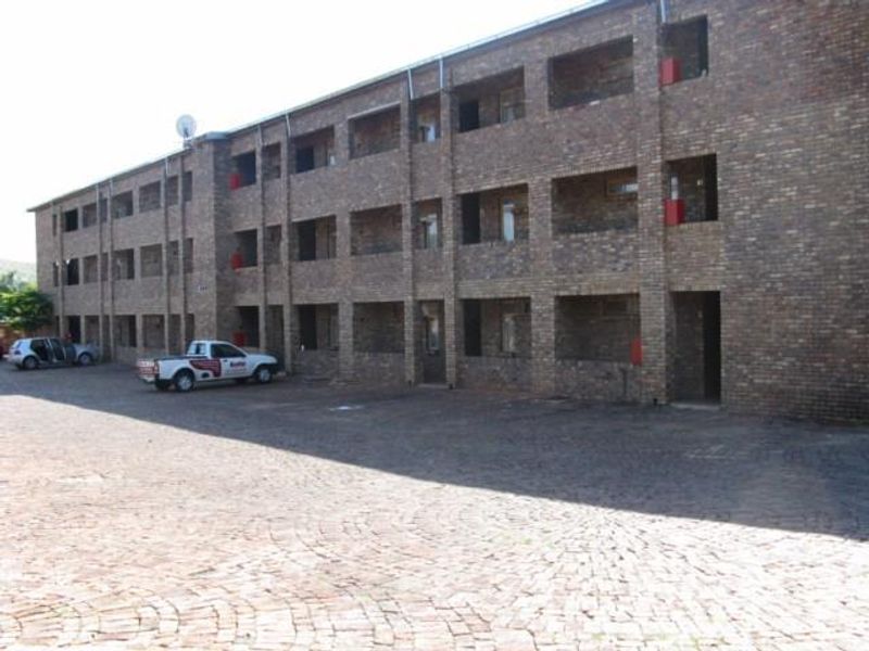 A multi-story apartment building featuring a face brick facade with integrated balconies and a paved parking area.