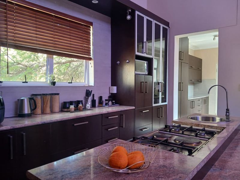 Modern kitchen featuring dark cabinetry, stone countertops, integrated hob, and a secondary scullery area visible through the doorway.