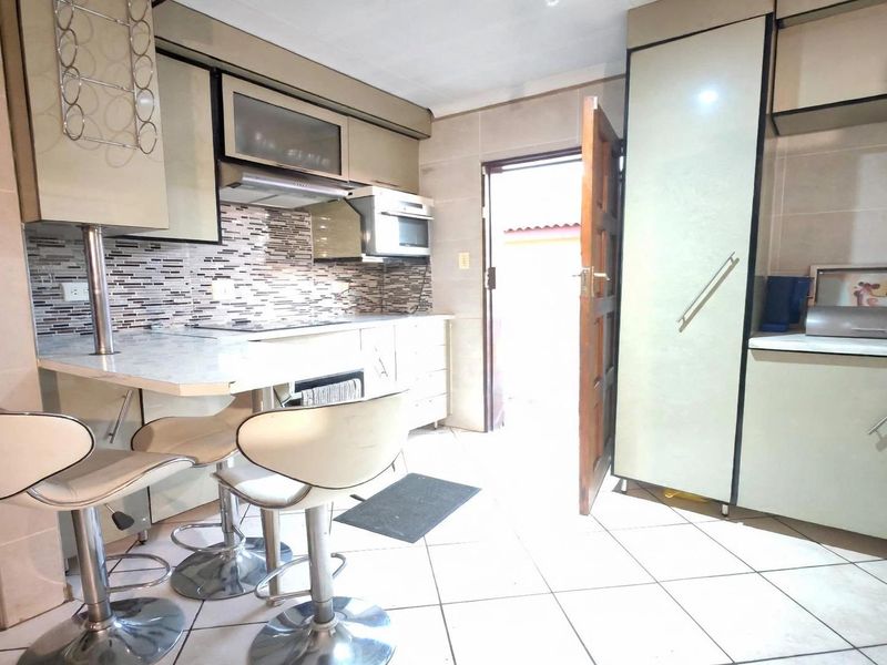 A functional kitchen featuring built-in cabinetry, a mosaic tile backsplash, tiled flooring, and a breakfast counter, with direct access to the exterior.