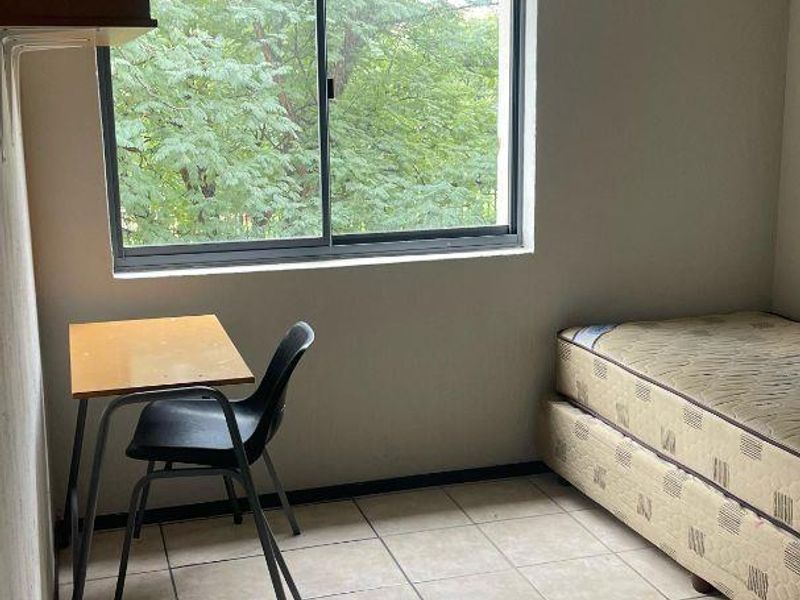 A simple bedroom featuring tiled flooring and a sliding window with a view of surrounding trees.