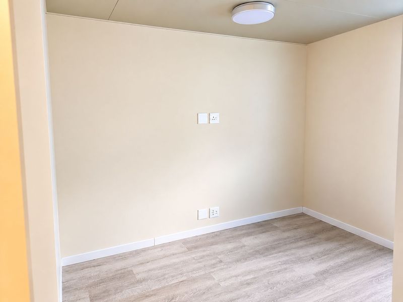A clean, empty bedroom featuring neutral walls, modern laminate flooring, and a flush-mount ceiling light fixture.