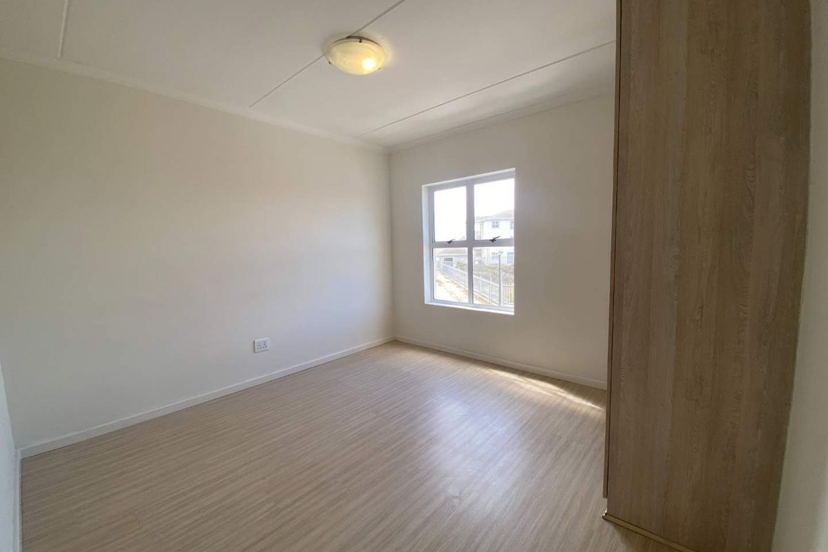 A bright, empty bedroom featuring light wood-look flooring, a built-in wardrobe, and a window providing natural light.