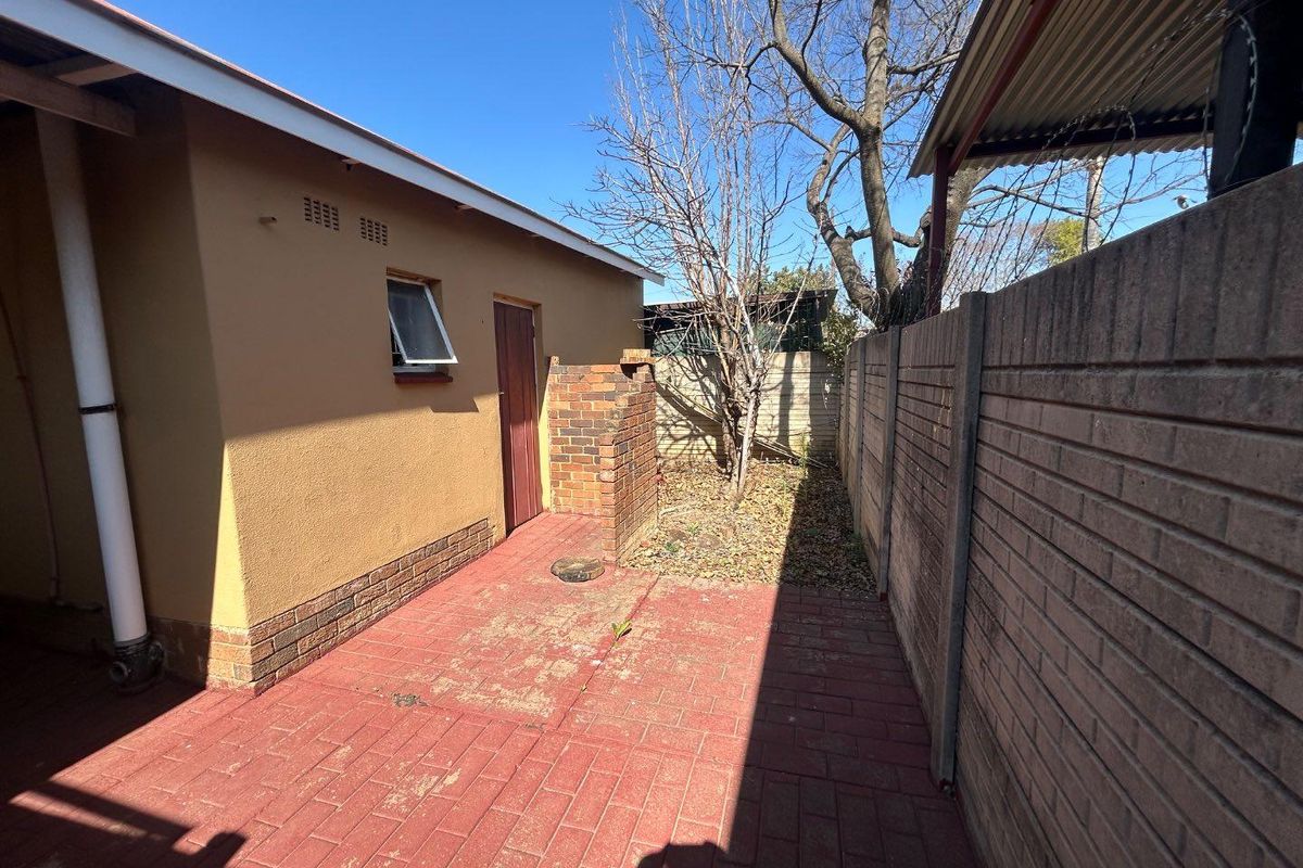 A side exterior area featuring paved flooring, a brick boundary wall, and a small utility access point along the side of the house.