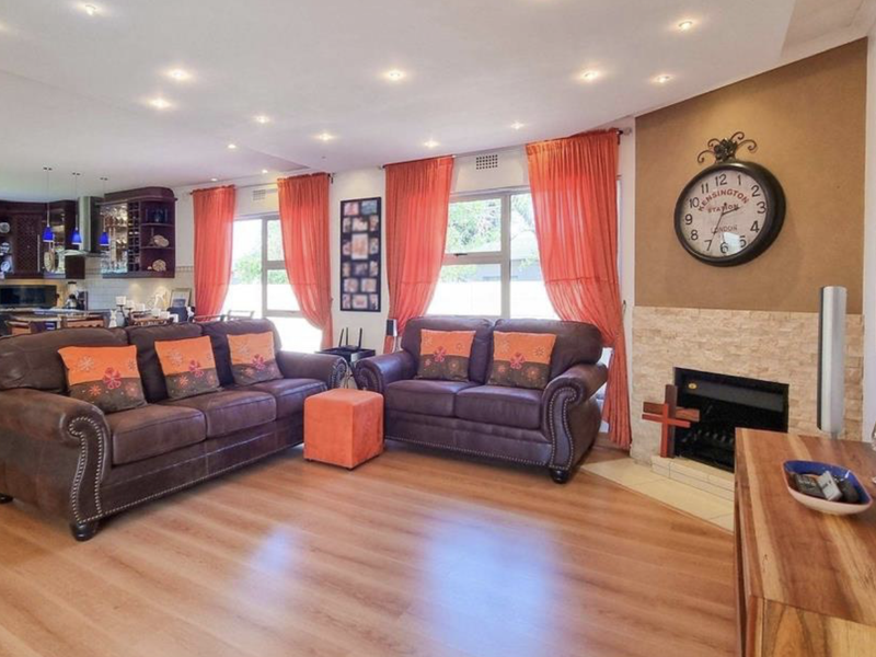 Spacious open-plan living area featuring laminate flooring, a stone-clad fireplace, and a seamless transition into a well-appointed kitchen with built-in cabinetry.