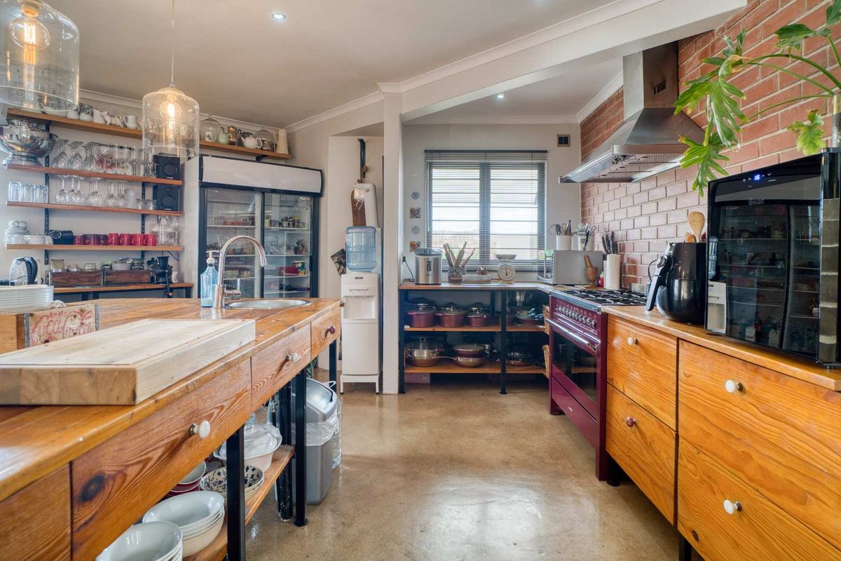 A rustic-style kitchen featuring a large wooden island, exposed brick wall, stainless steel extractor fan, and polished concrete flooring.