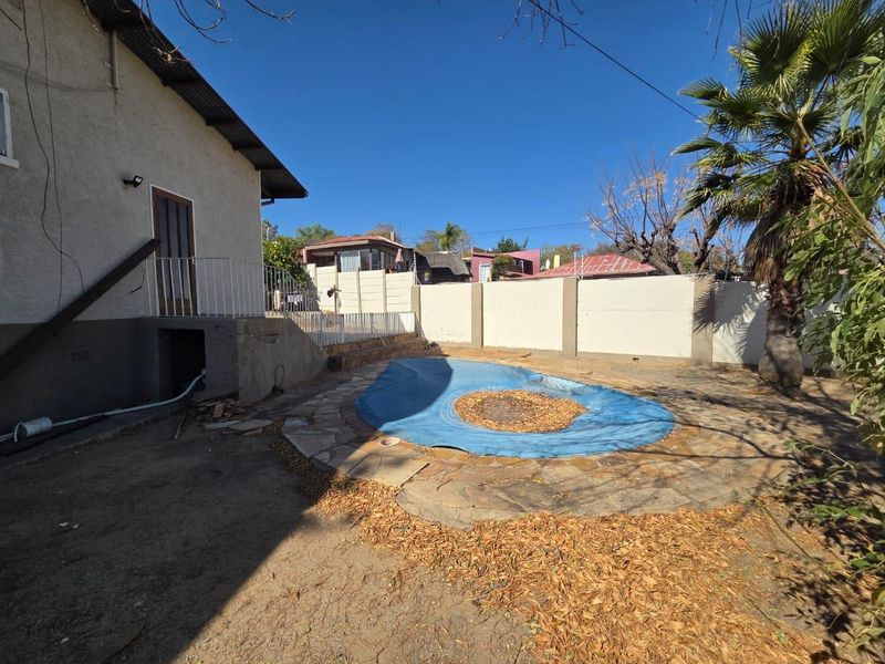 Rear garden area featuring a swimming pool with a cover, stone paving, and perimeter walling, requiring landscaping and maintenance.