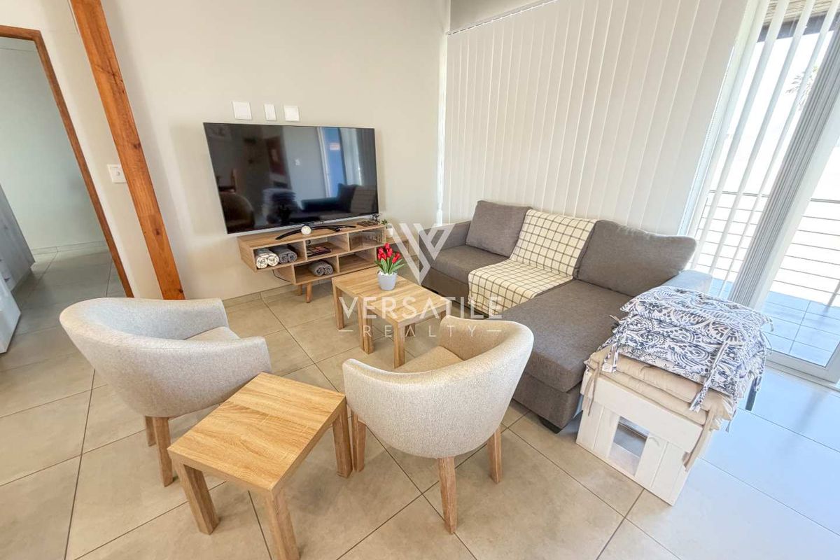 A bright living room featuring neutral tiled flooring, vertical blinds, and a sliding glass door providing access to the outdoor area.