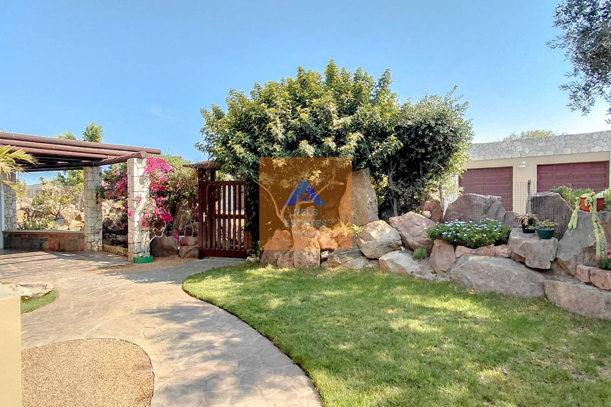 A well-maintained rear garden featuring a stone paved pathway, timber pergola, and natural stone landscaping elements.