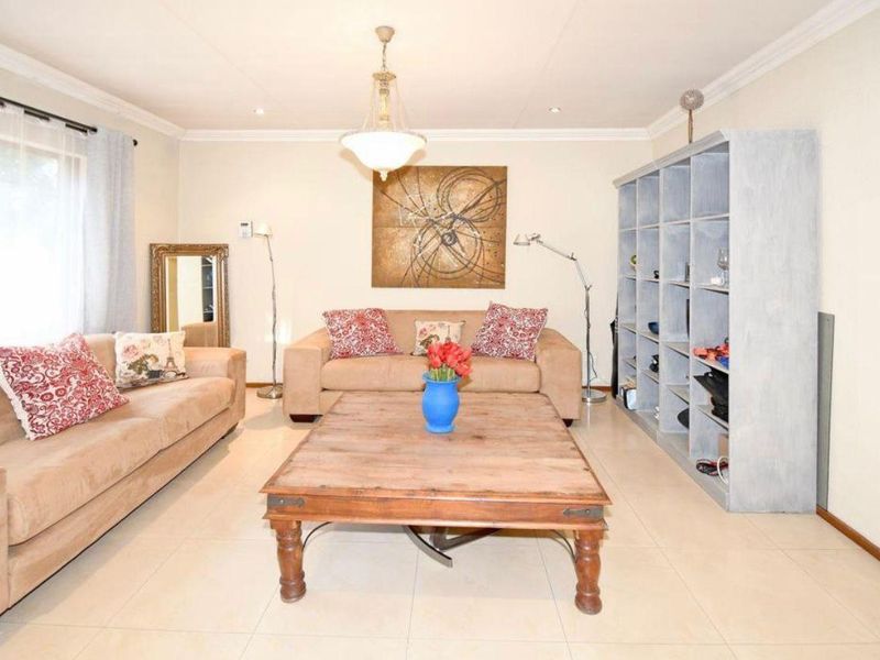 A well-lit living room featuring neutral tiled flooring, cove cornicing, and a central pendant light fixture, providing a comfortable and functional living space.