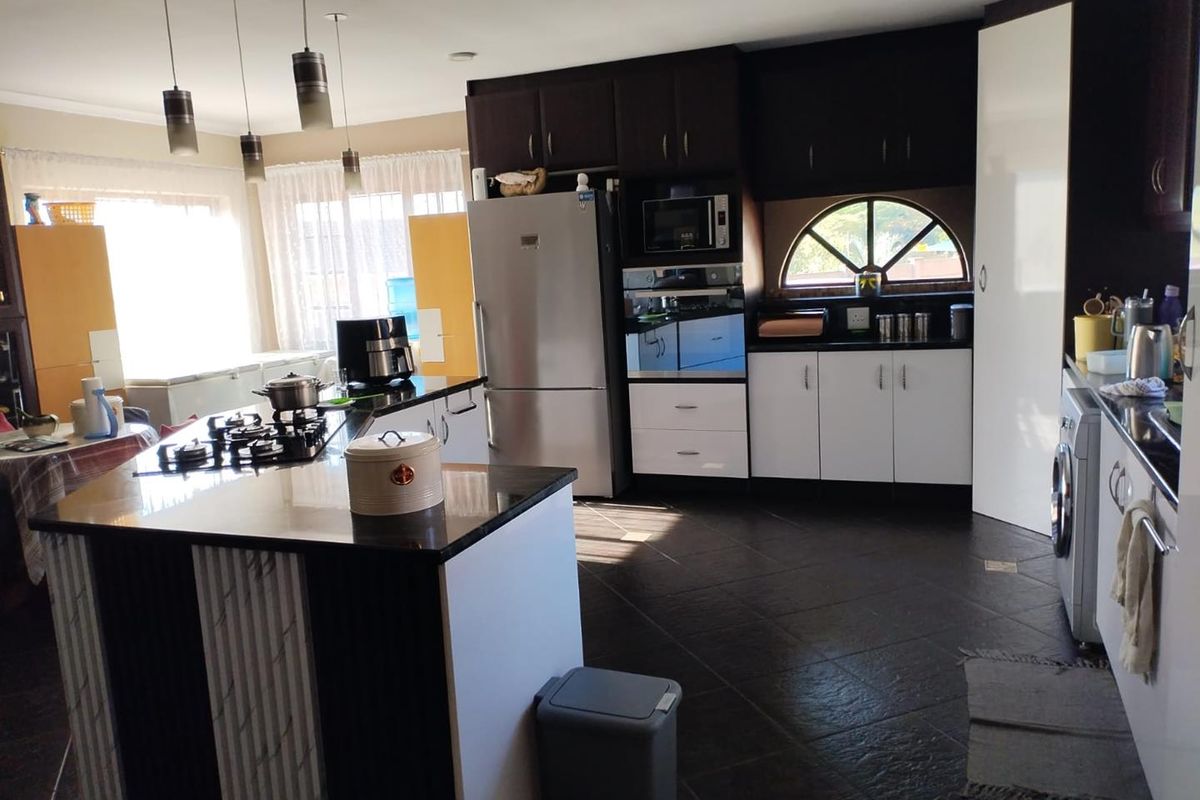 Modern kitchen featuring a central island with a gas hob, dark cabinetry, granite countertops, and a built-in oven with a microwave.