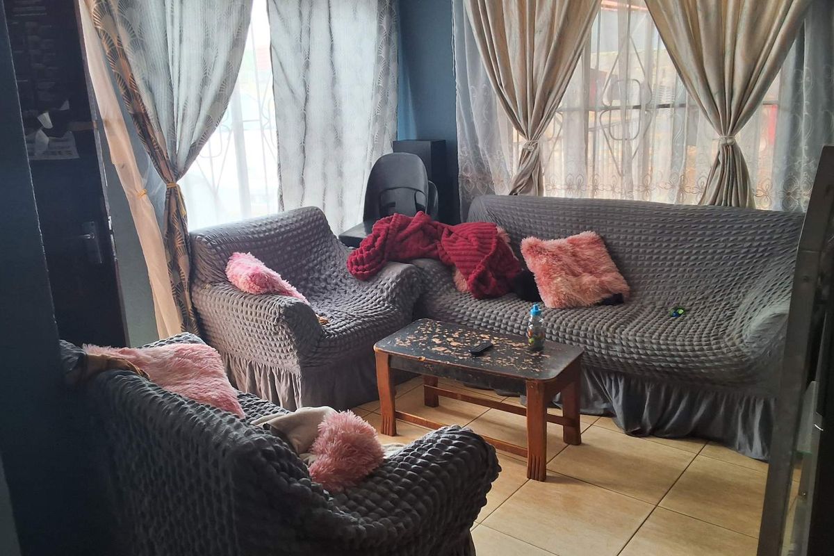 A living room area featuring tiled flooring and large windows with curtains, providing natural light to the space.