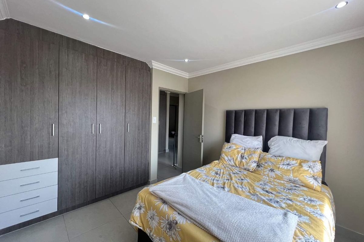 A well-maintained bedroom featuring modern built-in cupboards, tiled flooring, and recessed downlighting, offering a clean and functional living space.