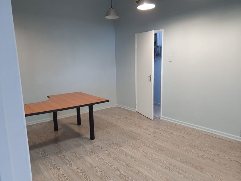 A clean, empty office space featuring light-toned laminate flooring, neutral walls, and modern pendant lighting, providing a versatile workspace environment.