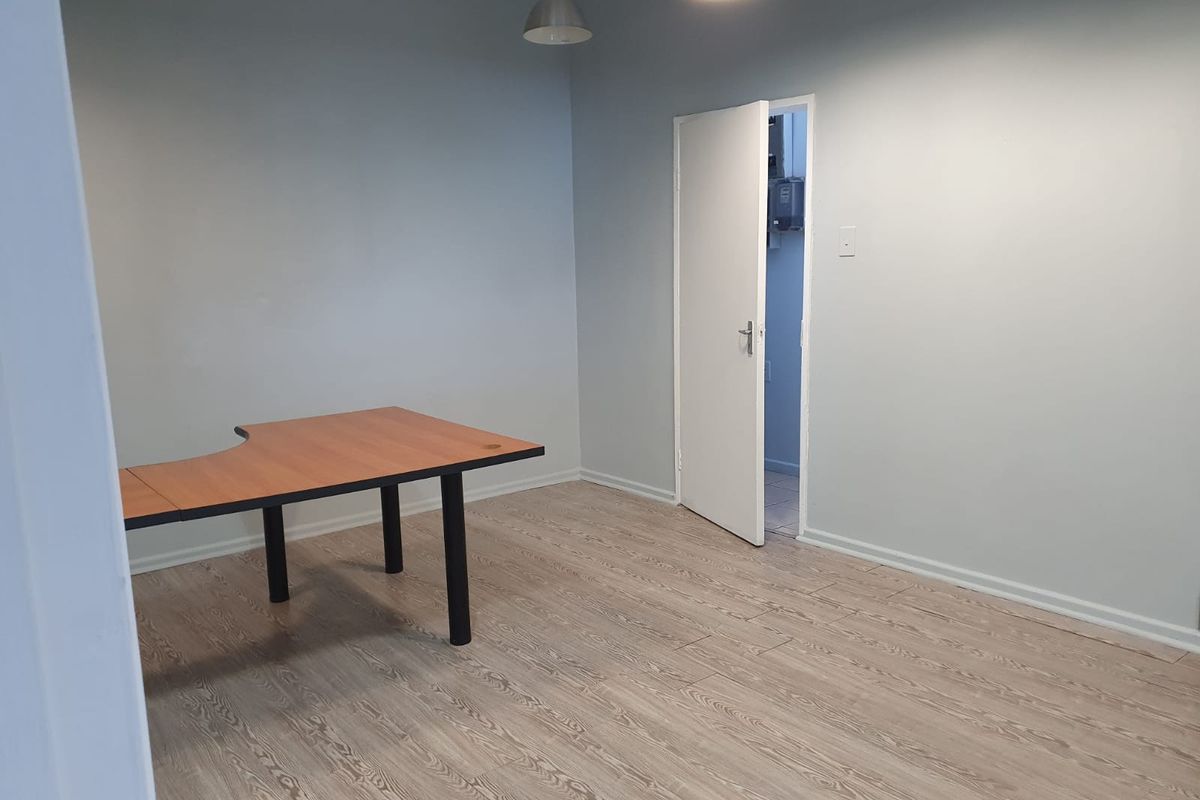 A clean, empty office space featuring light-toned laminate flooring, neutral walls, and modern pendant lighting, providing a versatile workspace environment.