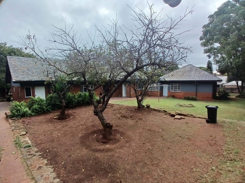A view of the rear exterior of the property featuring a brick facade, pitched roof, and a garden area with mature trees.
