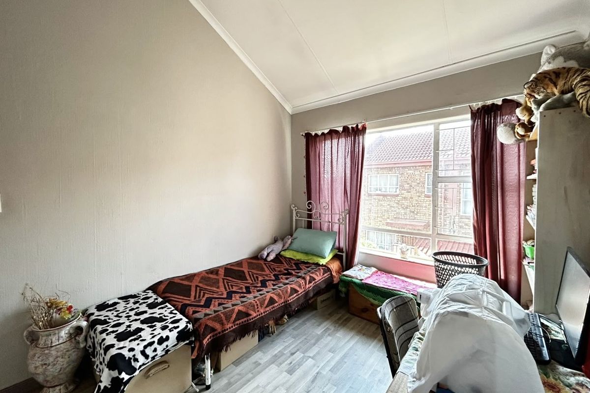 A bedroom featuring a large window with security bars and a high coved ceiling, providing natural light and a functional living space.