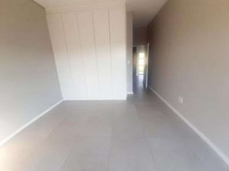 A bright, empty bedroom featuring neutral tiled flooring and modern built-in cupboards, offering a clean and versatile space.