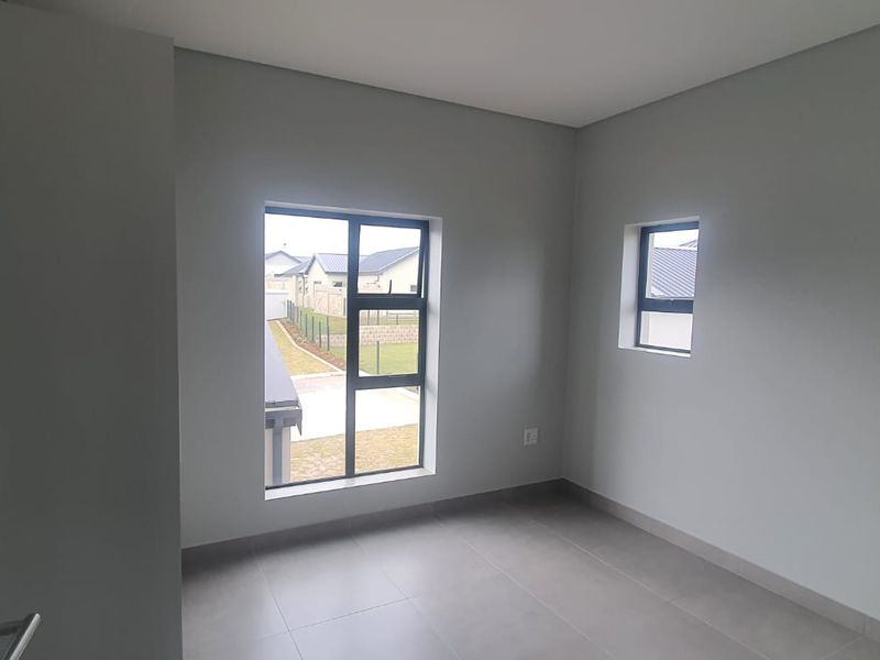 A bright, empty bedroom featuring neutral wall paint, modern tiled flooring, and aluminium-framed windows providing natural light.