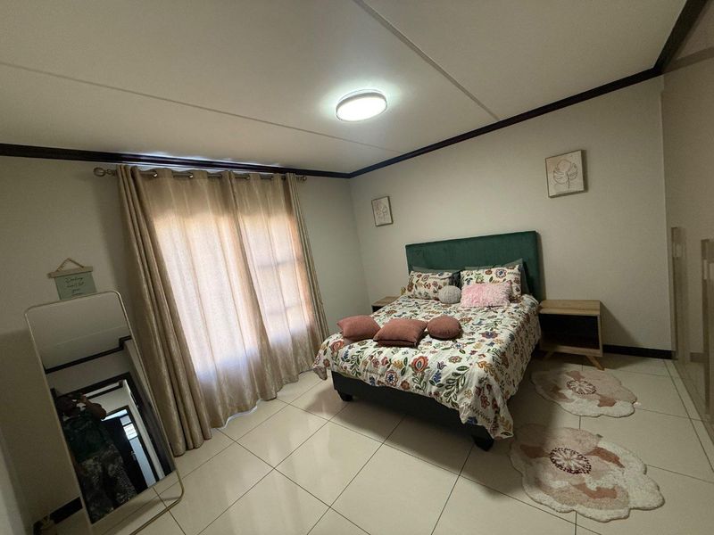 A well-maintained bedroom featuring neutral tiled flooring, a central ceiling light, and large windows dressed with curtains.