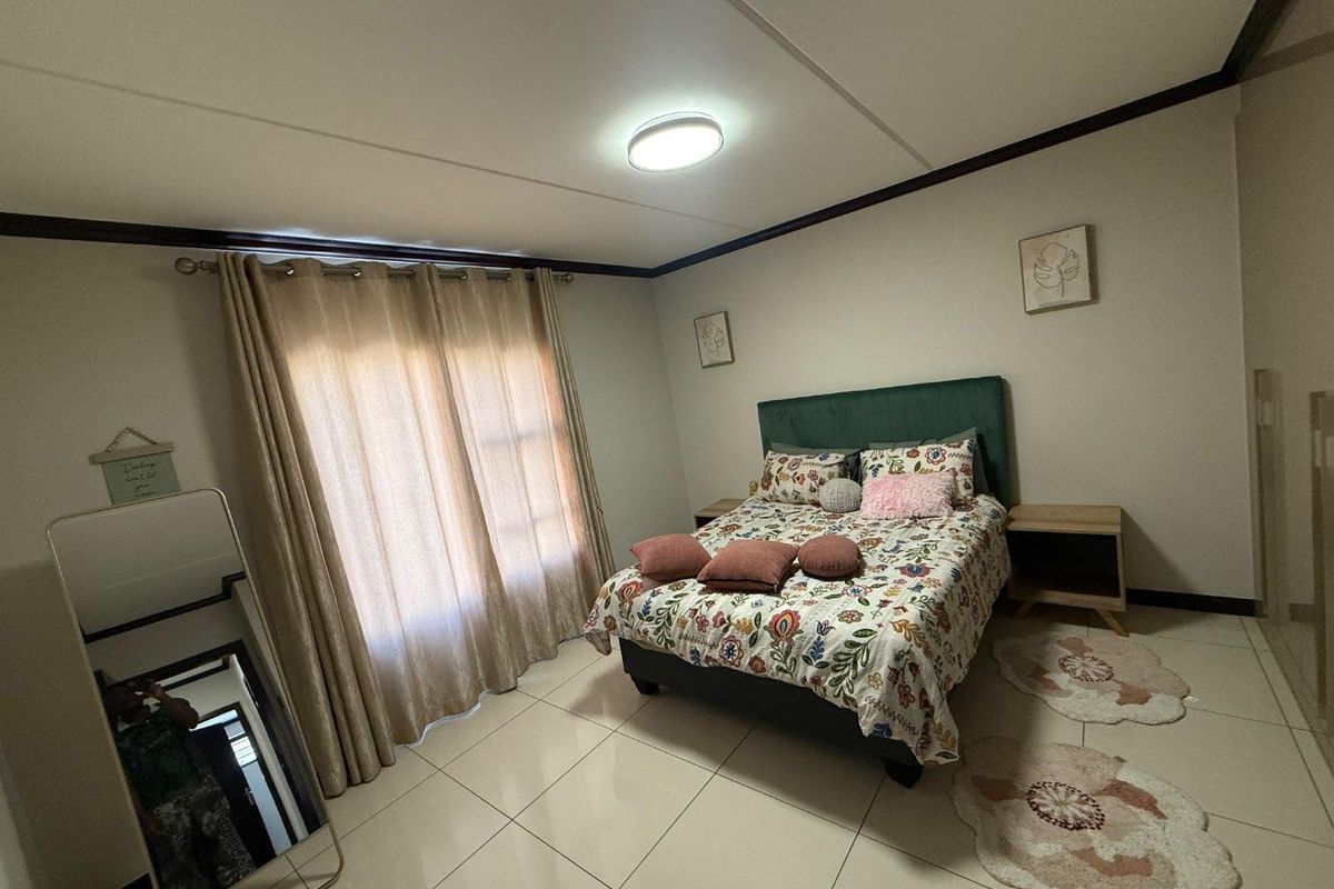 A well-maintained bedroom featuring neutral tiled flooring, a central ceiling light, and large windows dressed with curtains.