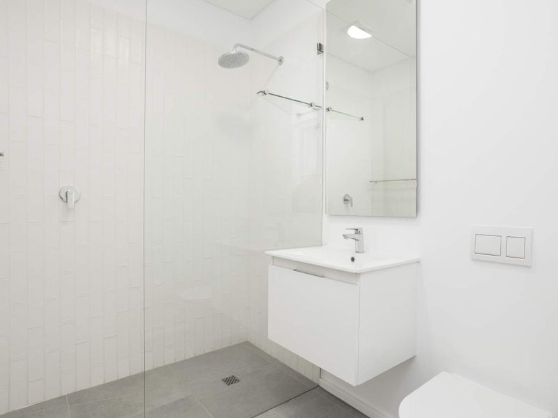 Modern bathroom featuring a wall-mounted vanity, glass shower screen with rain shower head, and a wall-hung toilet with clean white tiling.