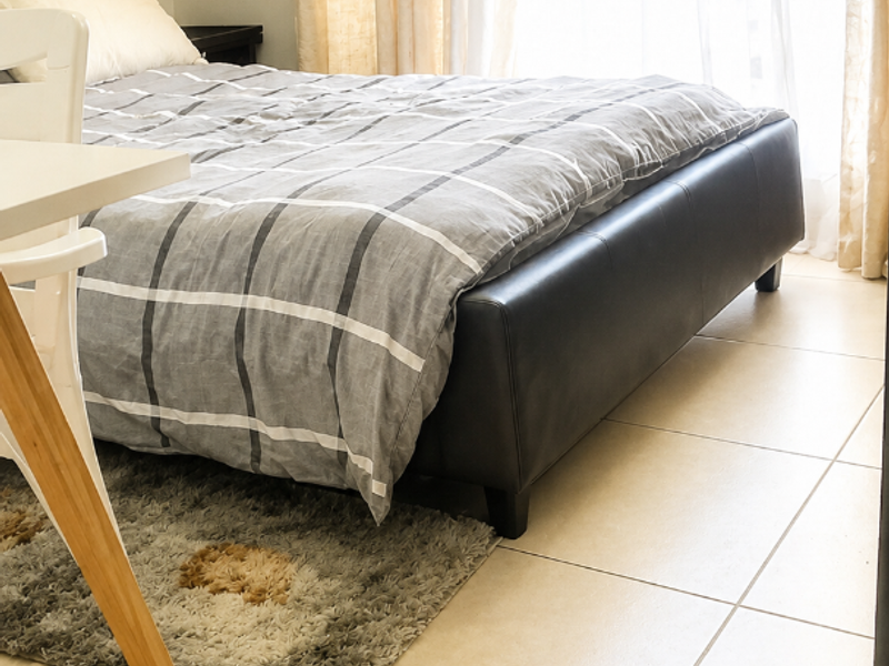 A bright bedroom featuring neutral tiled flooring and a large window with natural light, providing a clean and functional living space.