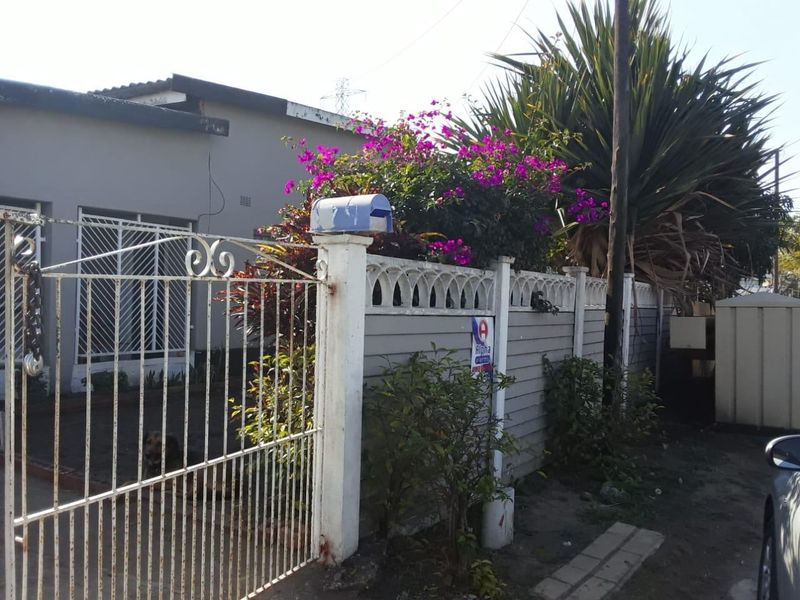 Front exterior view of the property featuring a metal security gate, precast concrete boundary wall, and established garden foliage.