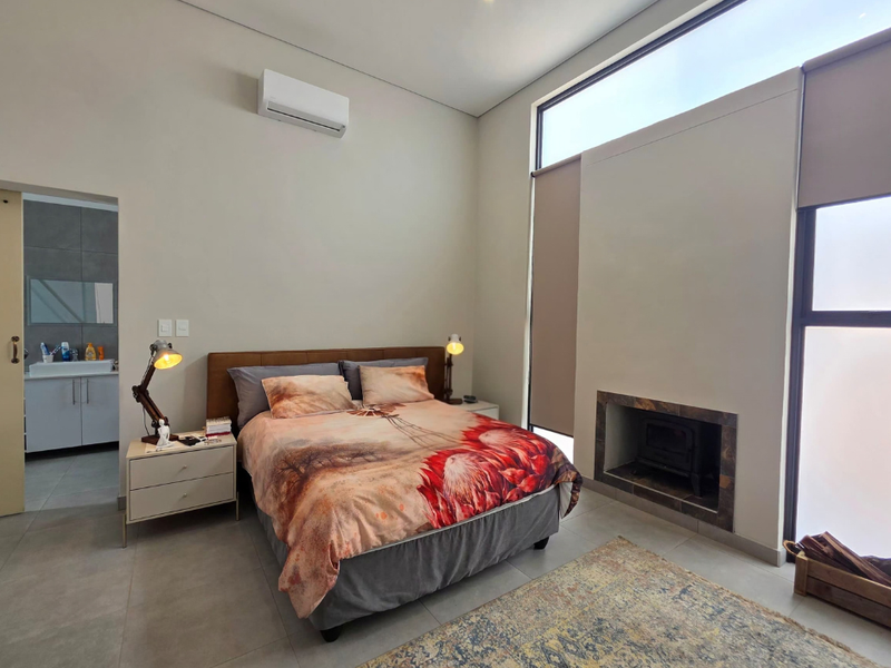 Modern bedroom featuring a built-in fireplace, split-system air conditioning, large windows, and an en-suite bathroom with tiled flooring throughout.