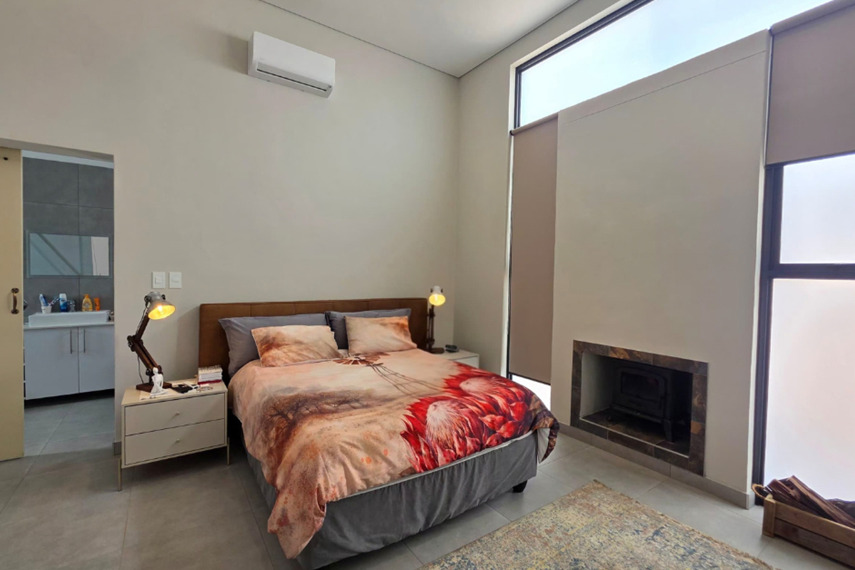 Modern bedroom featuring a built-in fireplace, split-system air conditioning, large windows, and an en-suite bathroom with tiled flooring throughout.
