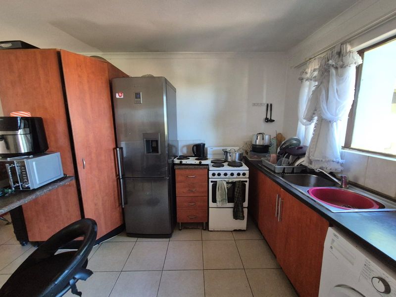 A functional kitchen featuring wood-look cabinetry, laminate countertops, a stainless steel sink, and a freestanding stove with tiled flooring.