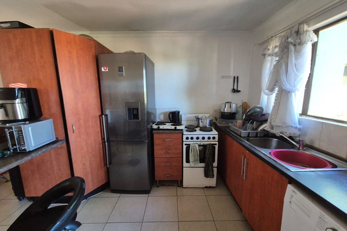 A functional kitchen featuring wood-look cabinetry, laminate countertops, a stainless steel sink, and a freestanding stove with tiled flooring.