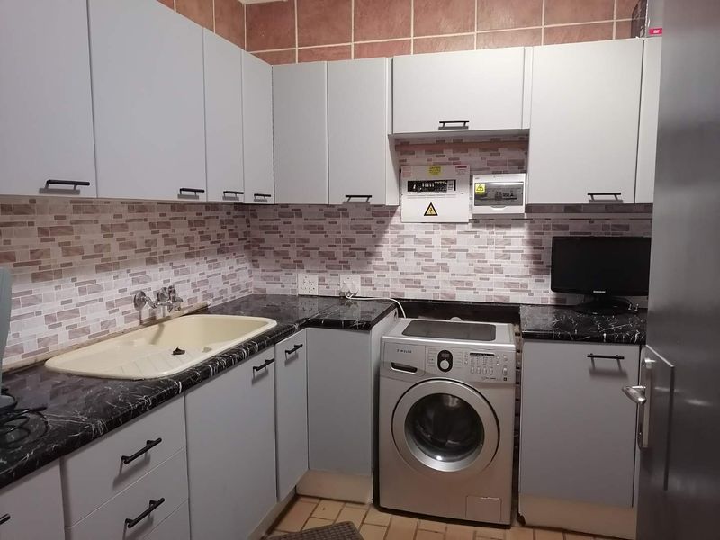 A functional laundry room featuring built-in cabinetry, a dark laminate countertop, a drop-in sink, and tiled backsplash with an integrated electrical distribution board.