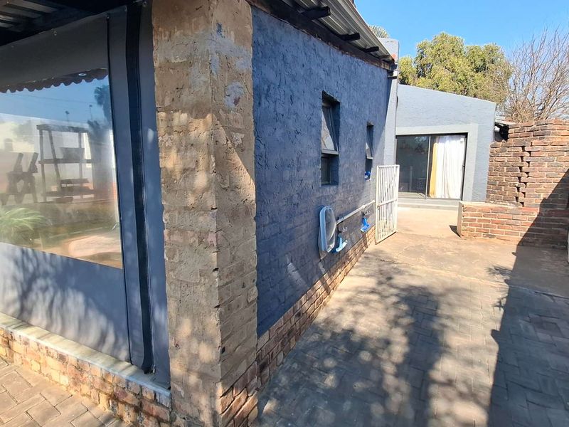 Rear exterior view showing a paved patio area, brick wall construction, and a sliding glass door leading into the home.