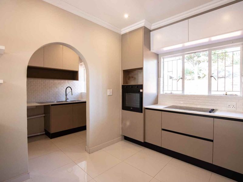 Modern kitchen featuring sleek cabinetry, built-in oven, hob, subway tile backsplash, and a convenient adjoining scullery area with a double sink.