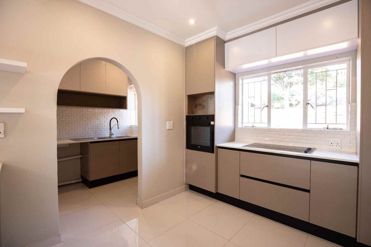 Modern kitchen featuring sleek cabinetry, built-in oven, hob, subway tile backsplash, and a convenient adjoining scullery area with a double sink.